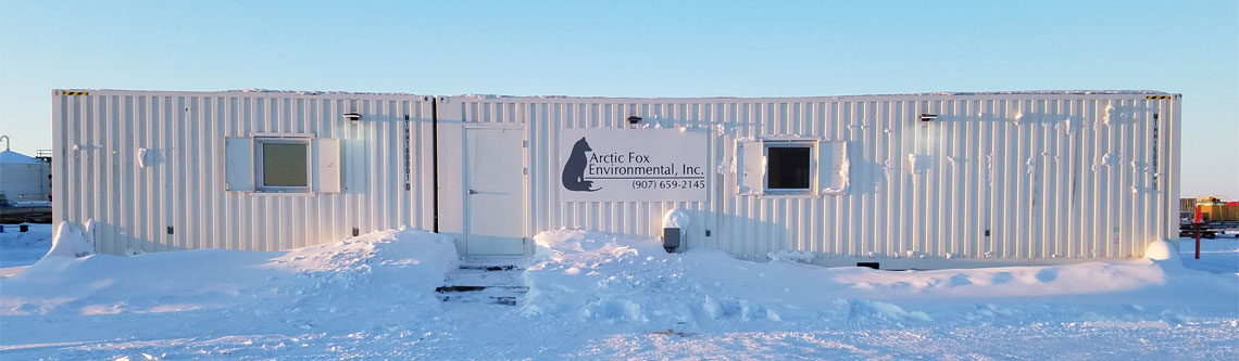Exterior view of the Arctic Fox Environmental, Inc. laboratory facility in Prudhoe Bay, Alaska, showing the modular industrial building surrounded by snow under a clear Arctic sky.